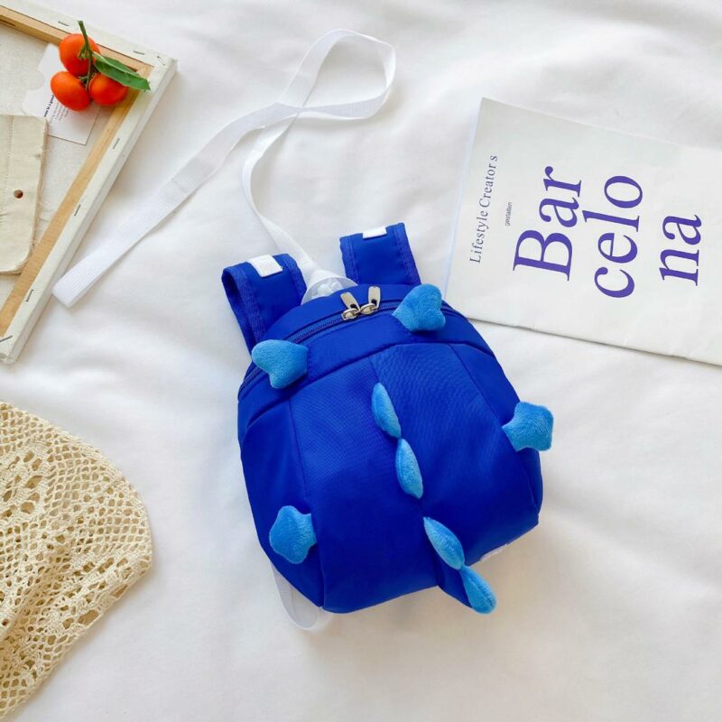 Mochila preescolar en forma de dinosaurio azul con fondo, cama blanca, cartel con escritura azul