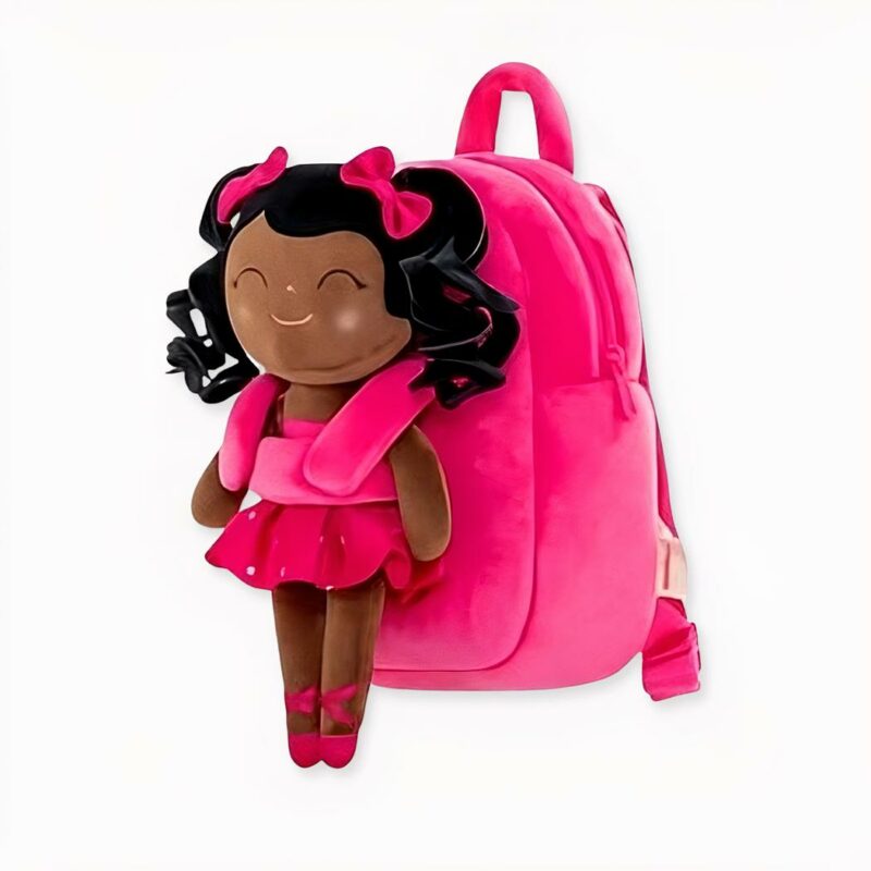 mochila infantil de primer grado, rosa con un muñeco de peluche de una niña vestida de bailarina de ballet en la parte delantera. Es una joven de color, sonriente y con los ojos cerrados.