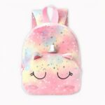 Mochila unicornio en rosa pastel, amarillo y azul. Los ojos del unicornio están en el bolsillo delantero de la bolsa, ella cierra los ojos, y sobre ellos están sus orejas y su cuerno plateado. El material de la bolsa es de felpa y hay estrellas plateadas por todas partes. El fondo es gris claro.