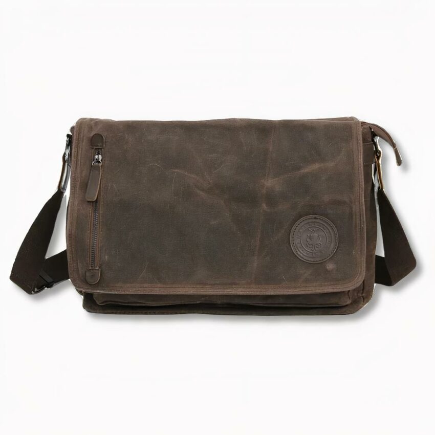 Cartera de estudiante de lona marrón con bandolera y cremallera frontal izquierda, sobre fondo gris claro