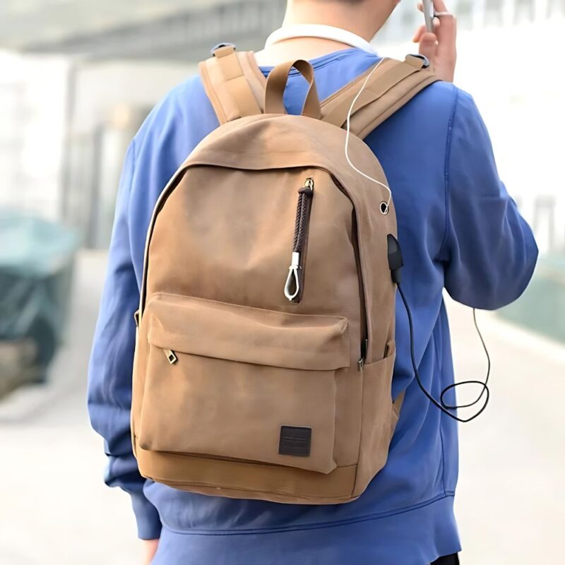 Jeune homme portant le grand sac à dos chargeur USB sur son dos. IL est en train d etéléphoner tandis que son téléphoen se recharge tout seul sur la prise USB de son sac.