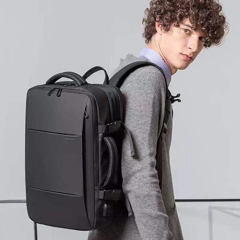 Un joven lleva al hombro una mochila rectangular negra. La bolsa tiene una cremallera en la parte superior y un asa a ambos lados.